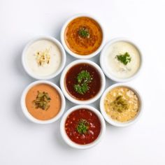 six small bowls filled with different types of sauces and condiments on a white surface