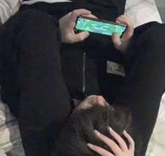 a person laying on top of a bed holding a cell phone in their hand and looking at the screen