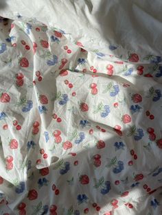 an unmade bed with white sheets and red flowers on the sheet cover is shown