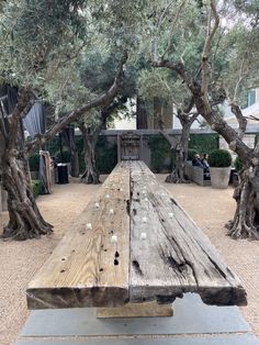 an old wooden picnic table in the middle of a park with trees and people sitting on benches