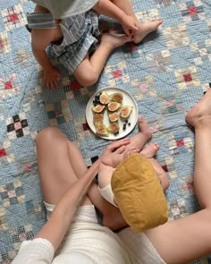 two people sitting on a bed with plates of food in front of them and one person holding a plate