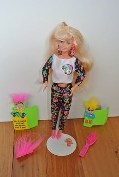 a doll with blonde hair standing on a wooden floor next to other dolls and accessories