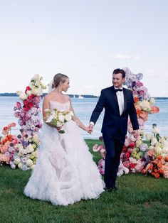 a bride and groom holding hands in front of an arch of flowers on the grass