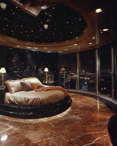 a large bed sitting in the middle of a room next to a window with city lights on it