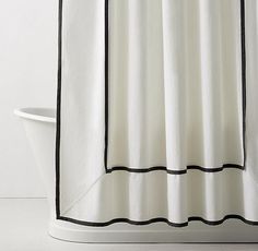 a white bath tub sitting next to a shower curtain with black trim on the edges