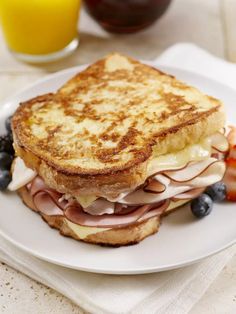 a toasted sandwich with ham, cheese and blueberries on a plate next to orange juice