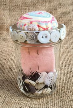 a jar filled with buttons sitting on top of a burlied cloth covered floor