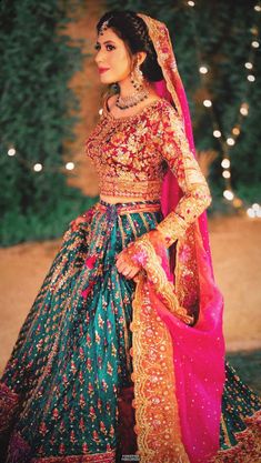 a woman in a green and pink wedding dress standing on the ground with lights behind her