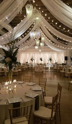 a banquet hall with white drapes and chandeliers hanging from the ceiling over tables