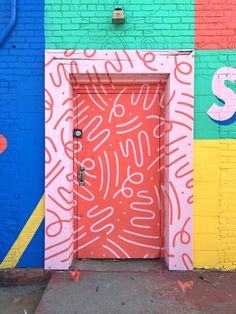 an orange door is in front of a colorful wall