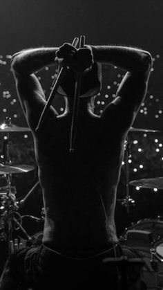 a man with his back to the camera on stage in front of drums and microphones