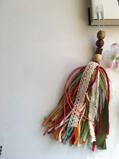 a colorful tassel hanging from the side of a white wall next to a flower