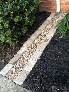 there is a brick wall and some plants in the front garden area with black mulch on the ground