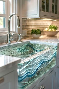 a glass sink in the middle of a kitchen with white cabinets and marble counter tops