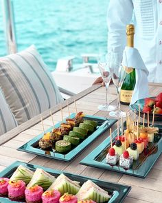 two trays filled with assorted appetizers on a table next to the ocean