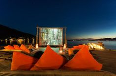 an outdoor movie is set up on the dock by the water with orange pillows and candles