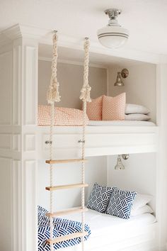 a white bunk bed with pink and blue pillows on top of it, hanging from the ceiling