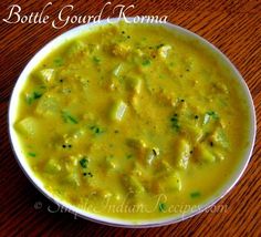 a white bowl filled with yellow soup on top of a wooden table next to a spoon