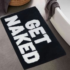 a bathroom rug with the words naked on it in white and black, next to a bathtub