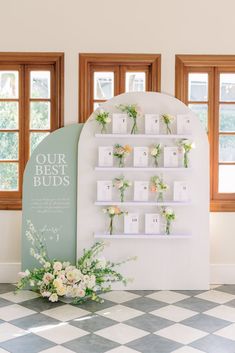 a display with flowers on it in front of two windows and a sign that says our best buds