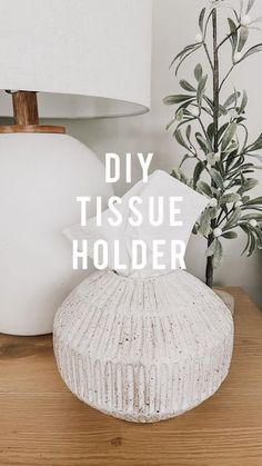 a white vase sitting on top of a wooden table next to a lamp and potted plant