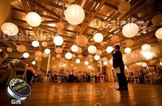 a man standing on top of a wooden floor under lots of white paper lanterns hanging from the ceiling