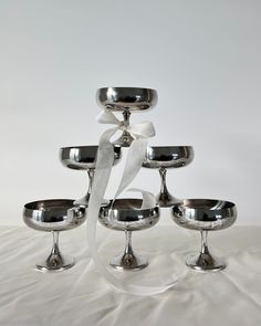 a stack of silver bowls sitting on top of a white table covered in ribbon and ribbons