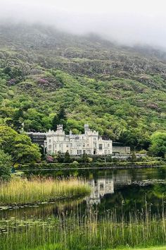 a large white house sitting on top of a lush green hillside next to a lake