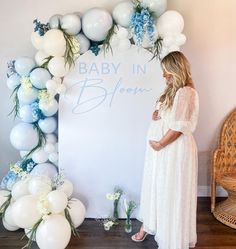 a pregnant woman standing in front of a backdrop with white and blue balloons that say baby in bloom