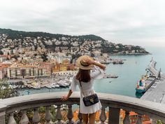 a woman standing on top of a balcony looking at the water and boats in the harbor