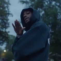 a man in a hoodie standing on the street with his hands up and looking at something