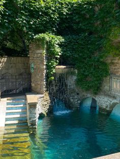 an outdoor swimming pool surrounded by greenery and stone steps leading up to the water