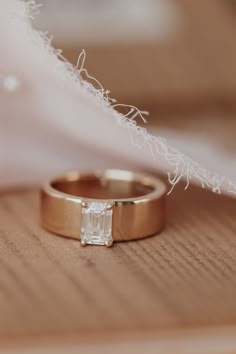 a wedding ring with an emerald cut diamond on it sitting on top of a wooden table