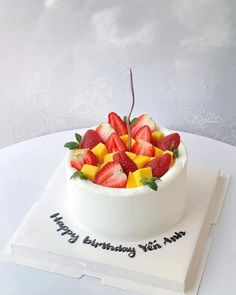 a birthday cake with strawberries and oranges in a bowl on a white plate