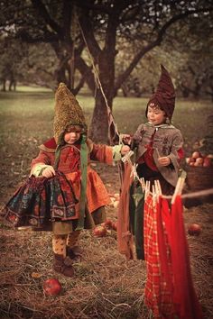 two children dressed up in costumes playing with an apple tree branch and apples on the ground