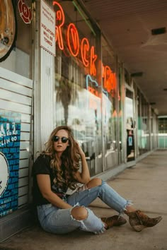 a woman sitting on the sidewalk in front of a rock shop with her legs crossed