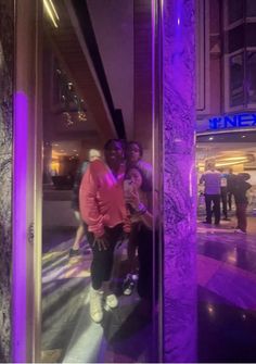 three people standing in front of a tall building with purple lights on it's sides