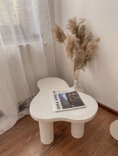 a white table with a magazine on it next to a vase filled with dried plants