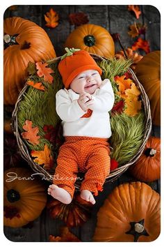 a baby is laying in a basket with pumpkins around him and smiling at the camera