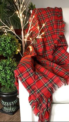 a red plaid blanket sitting on top of a white couch next to a potted plant