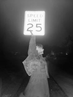 a person holding up a sign that says speed limit 25 on the street at night