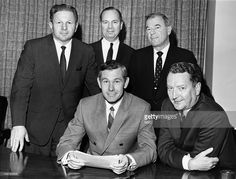 four men in suits and ties posing for the camera at a table with papers on it