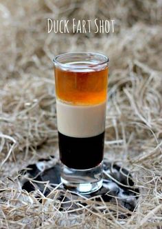 a shot glass filled with liquid sitting on top of dry grass next to the words duck far shot