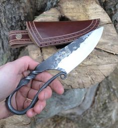 a person holding a knife in their hand next to a leather sheath on a tree stump