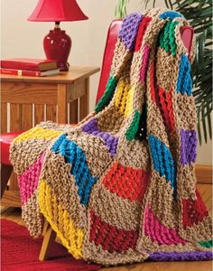 a crocheted blanket sitting on top of a wooden chair next to a red lamp