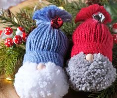 two knitted santa claus ornaments sitting on top of a wooden table next to pine cones