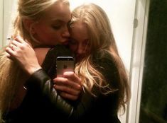 two women are hugging each other while looking at their cell phone in front of the mirror