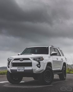 a white toyota suv parked on the side of a road under a dark cloudy sky