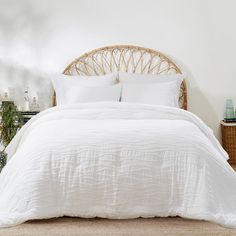 a bed with white linens and pillows in a small room next to a wicker headboard