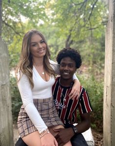 a man sitting on top of a woman's lap in front of some trees